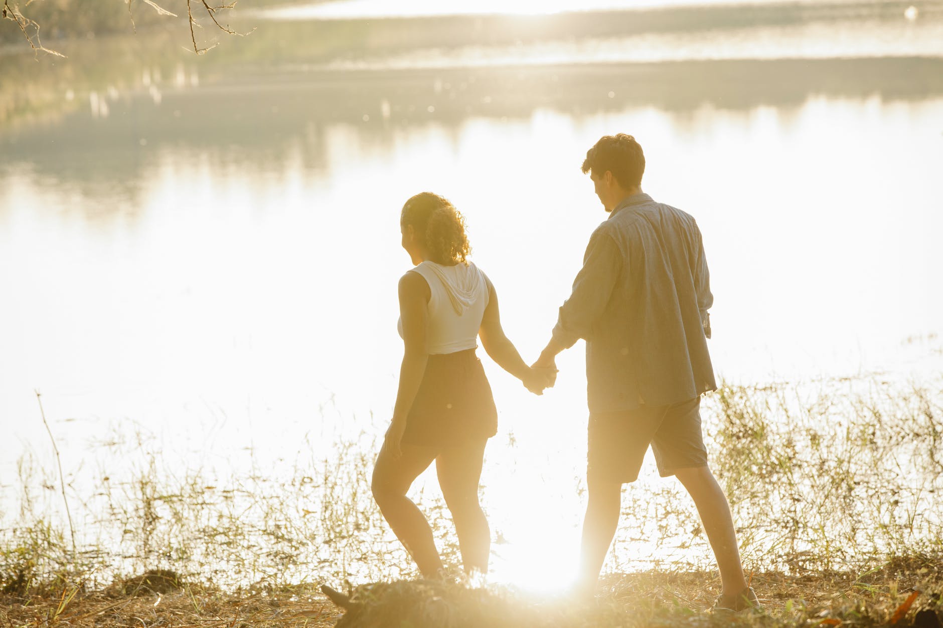 unrecognizable couple holding hands during stroll on lake coast